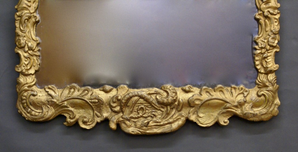 An 18th-century rectangular wall mirror featuring an intricate hand-carved giltwood frame adorned with rococo C-scrolls, foliage motifs, and a crest. View IV