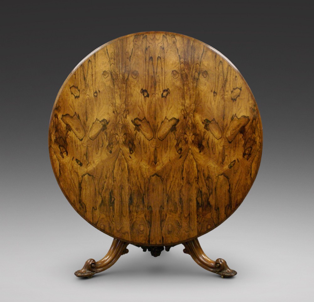 A circular rosewood centre table with a figured bookmatched veneered top shown tilted upright on a carved triform base.