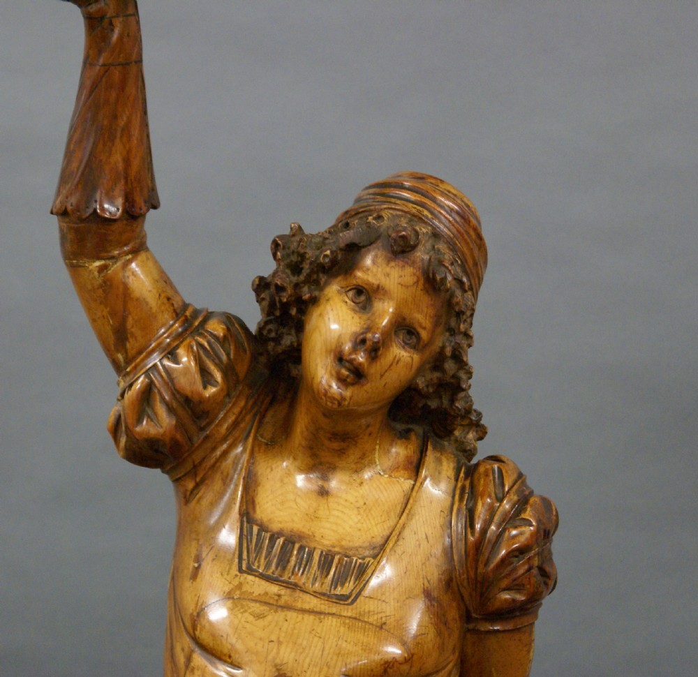 A carved wood figure of a standing youth holding a dish elevated overhead, set upon an ornate carved pedestal. View III