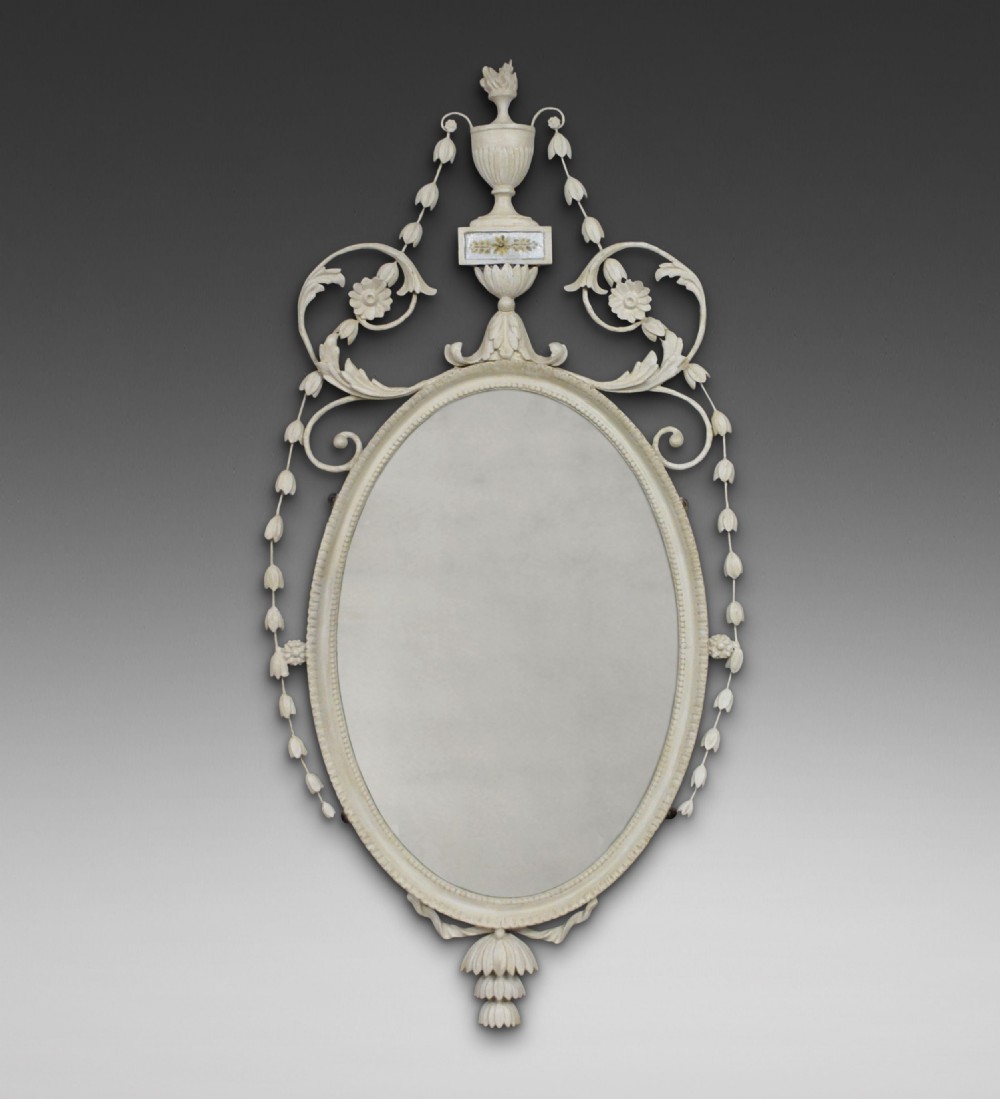An oval off-white painted Neoclassical wall mirror featuring an urn cresting, delicate floral swags, and decorative drop detail.