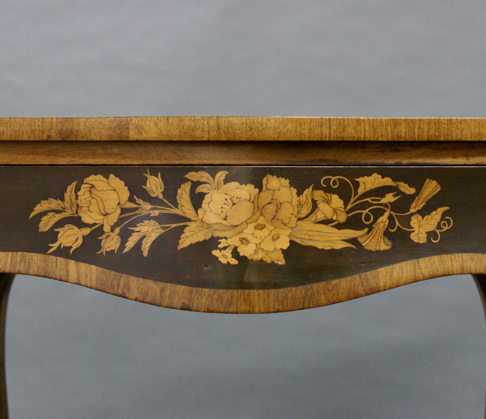 A French Rococo style writing table featuring curved cabriole legs, floral marquetry inlay on the dark apron, and a green leather inset top surface. View V