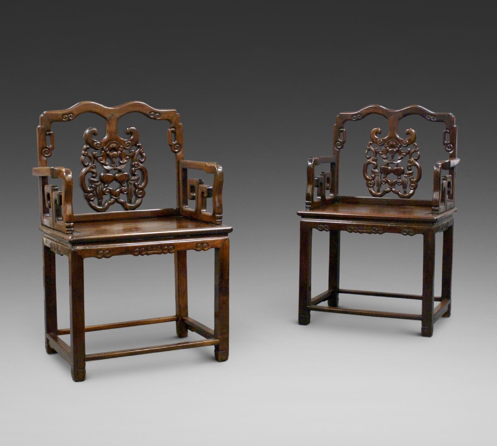 A pair of antique Chinese Qing dynasty dark hongmu armchairs featuring intricately carved openwork back splats and square mortise-and-tenon construction.