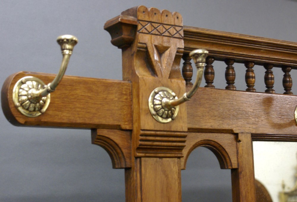 A Victorian oak hall stand featuring a central mirror, brass hooks, decorative tiles, a small marble shelf, and twin umbrella hoops above base drip trays. View II