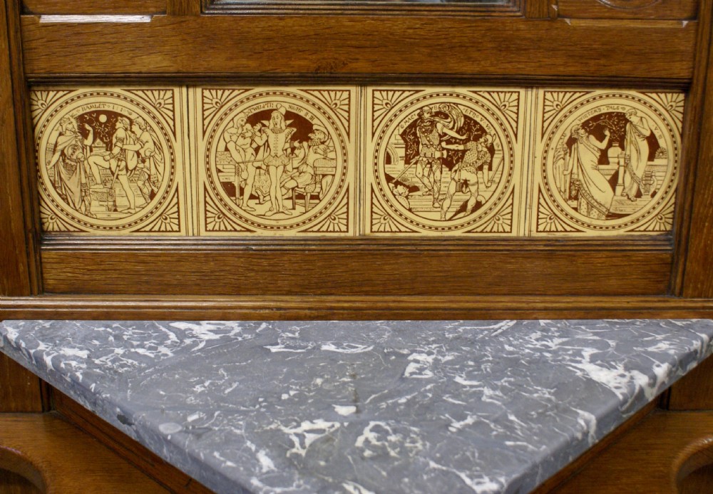 A Victorian oak hall stand featuring a central mirror, brass hooks, decorative tiles, a small marble shelf, and twin umbrella hoops above base drip trays. View VI