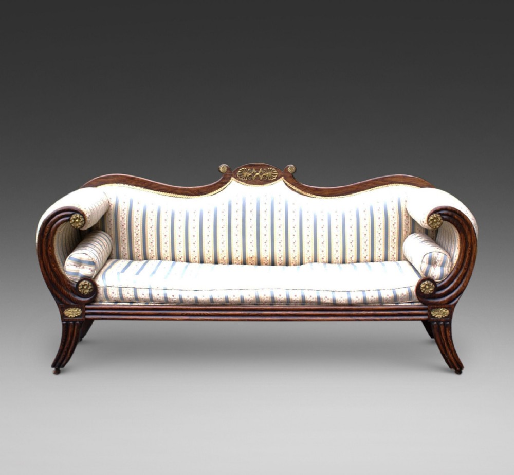 A Regency simulated rosewood sofa featuring scrolled arms with gilt brass rosettes, swept legs, and cream striped fabric upholstery.