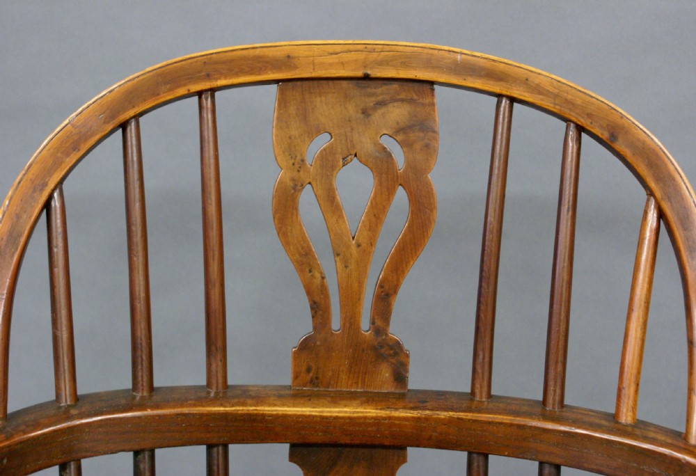 A warm brown antique Windsor armchair crafted from yew and elm, featuring a hoop back, pierced central splat, turned legs, and a curved stretcher. View V
