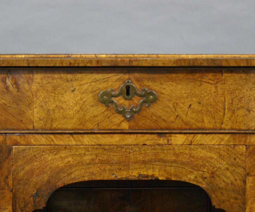 A George II figured walnut knee-hole desk featuring multiple drawers with brass batwing drop handles, raised on shaped bracket feet. View VI