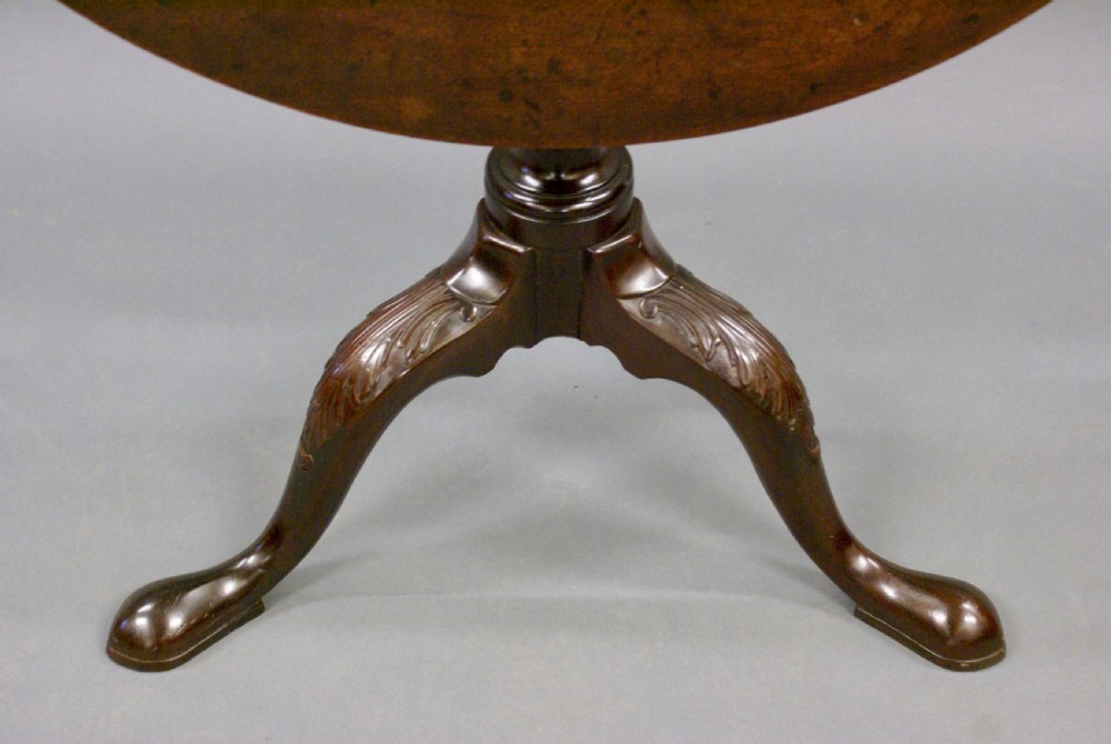 An antique Georgian dark mahogany tilt-top tripod table with a circular top raised vertically on a turned baluster stem and carved cabriole legs. View II