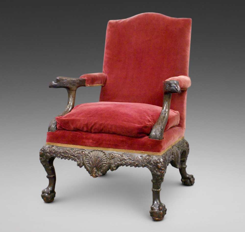 A Georgian style carved mahogany library armchair upholstered in red velvet with eagle head armrests and ball-and-claw feet.
