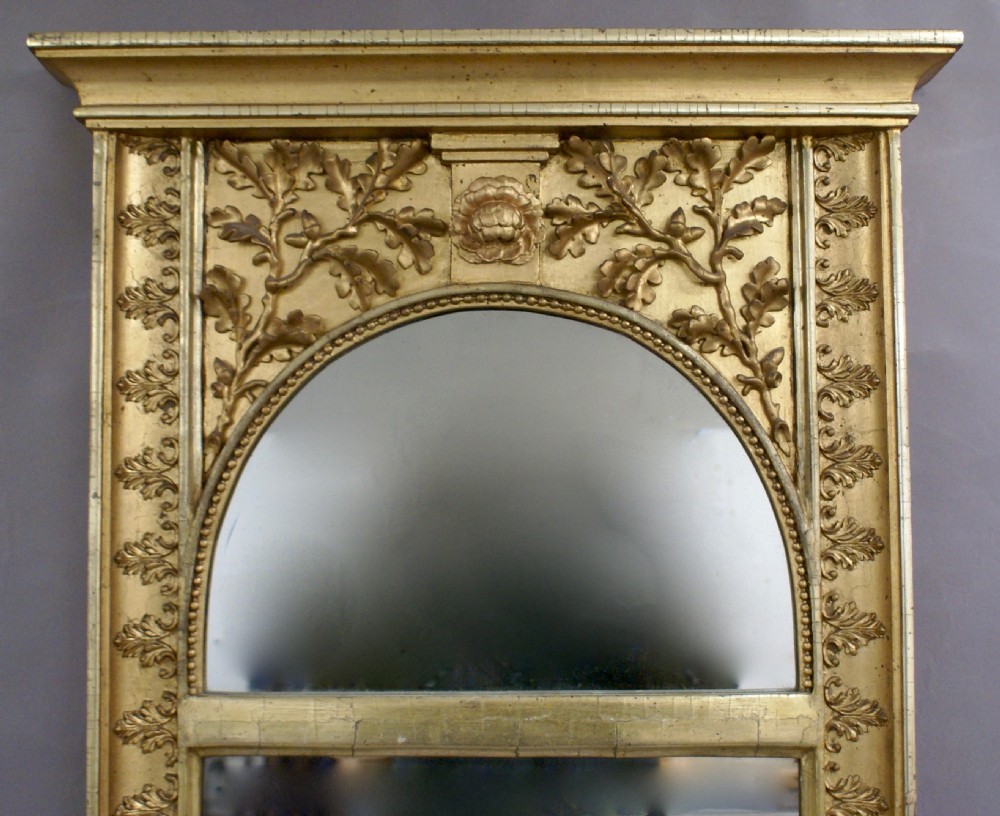 A tall, narrow early 19th-century French pier mirror featuring a gilded wood frame carved with oak leaves, an arched top plate, and a decorated lower plinth panel. View II