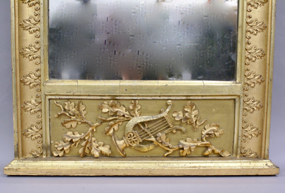 A tall, narrow early 19th-century French pier mirror featuring a gilded wood frame carved with oak leaves, an arched top plate, and a decorated lower plinth panel. View III
