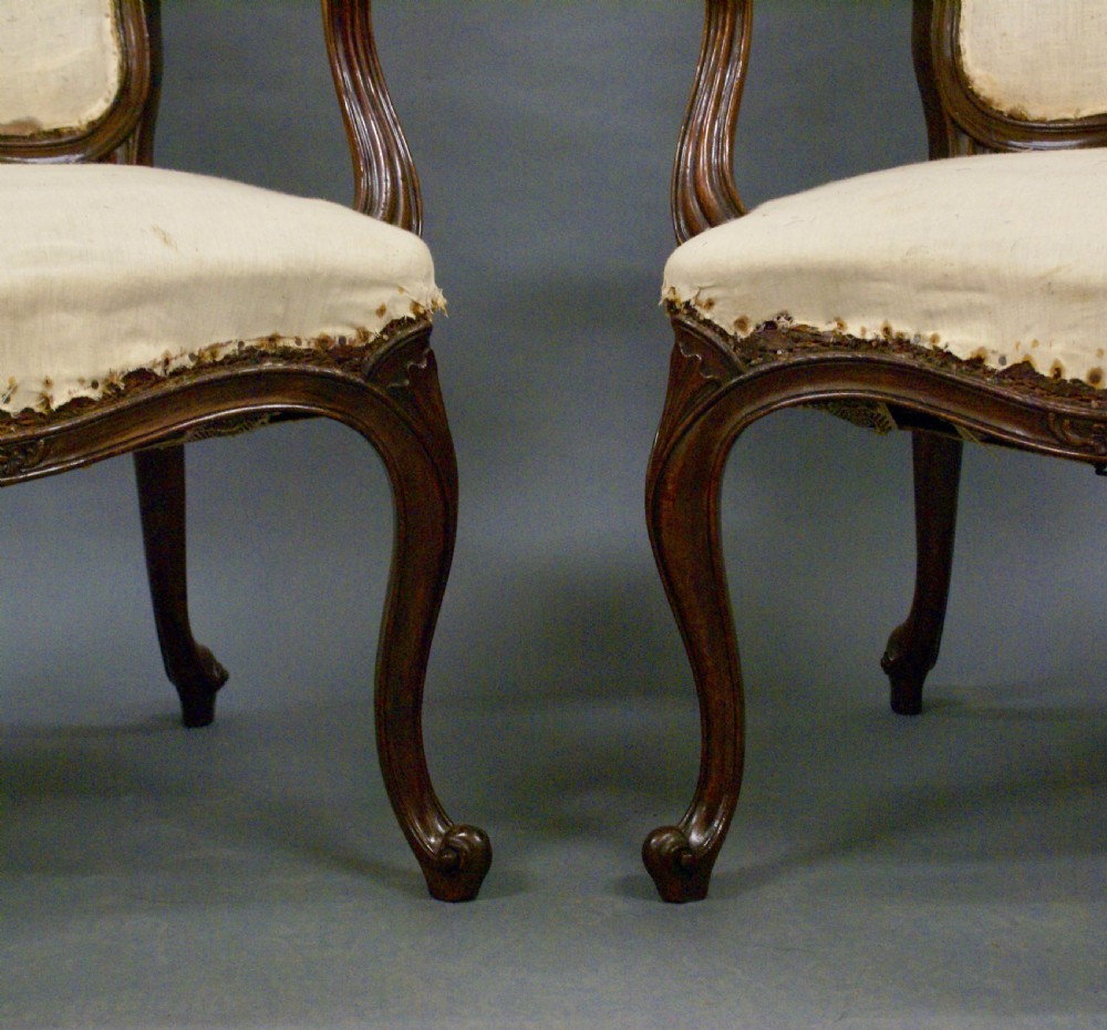 A pair of carved dark wood French Hepplewhite armchairs featuring cartouche backrests, padded armrests, and neutral cream fabric upholstery. View V