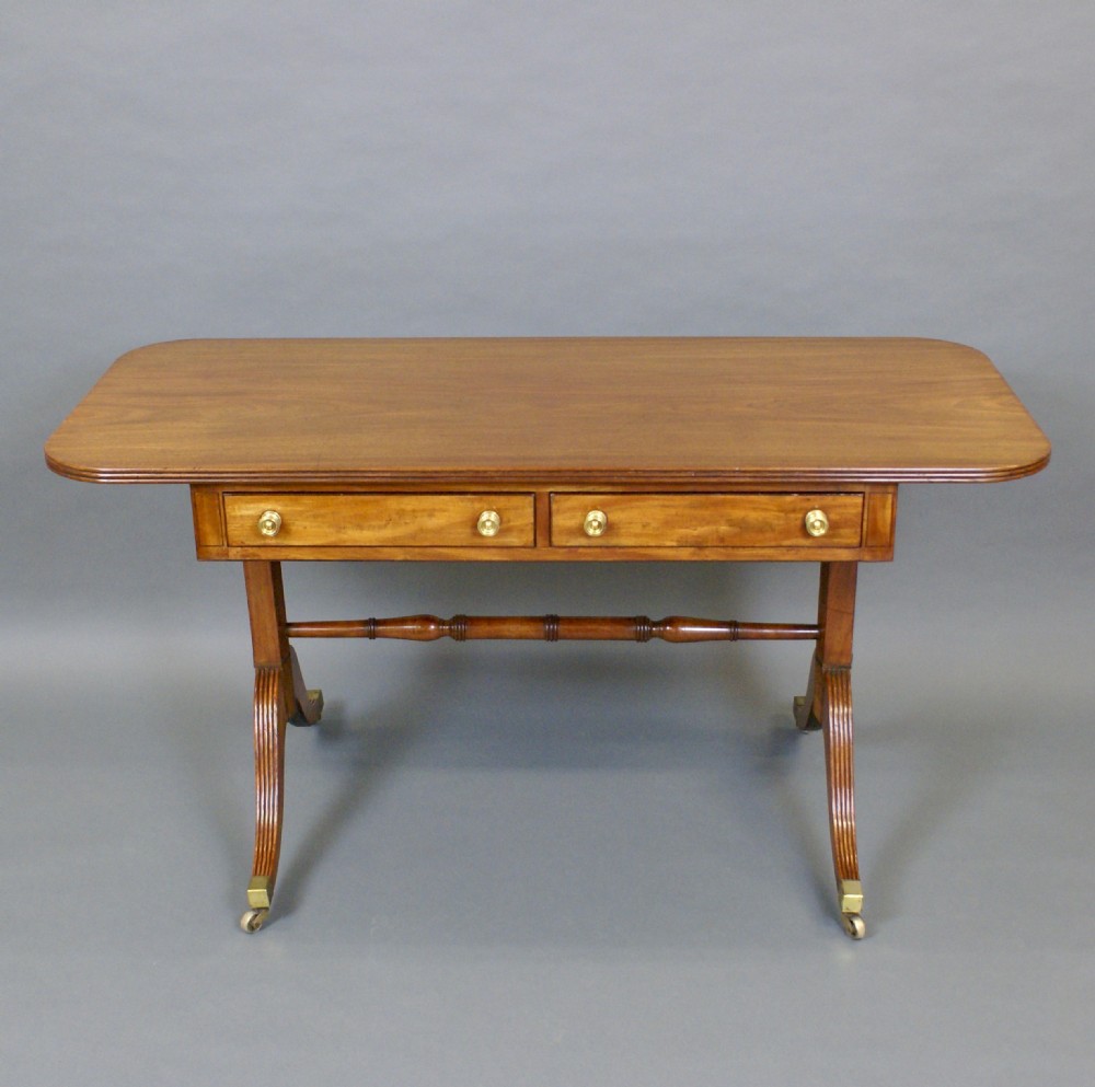A Regency mahogany sofa table featuring two frieze drawers with brass knobs, reeded sabre legs on brass castors, and a turned stretcher. View III