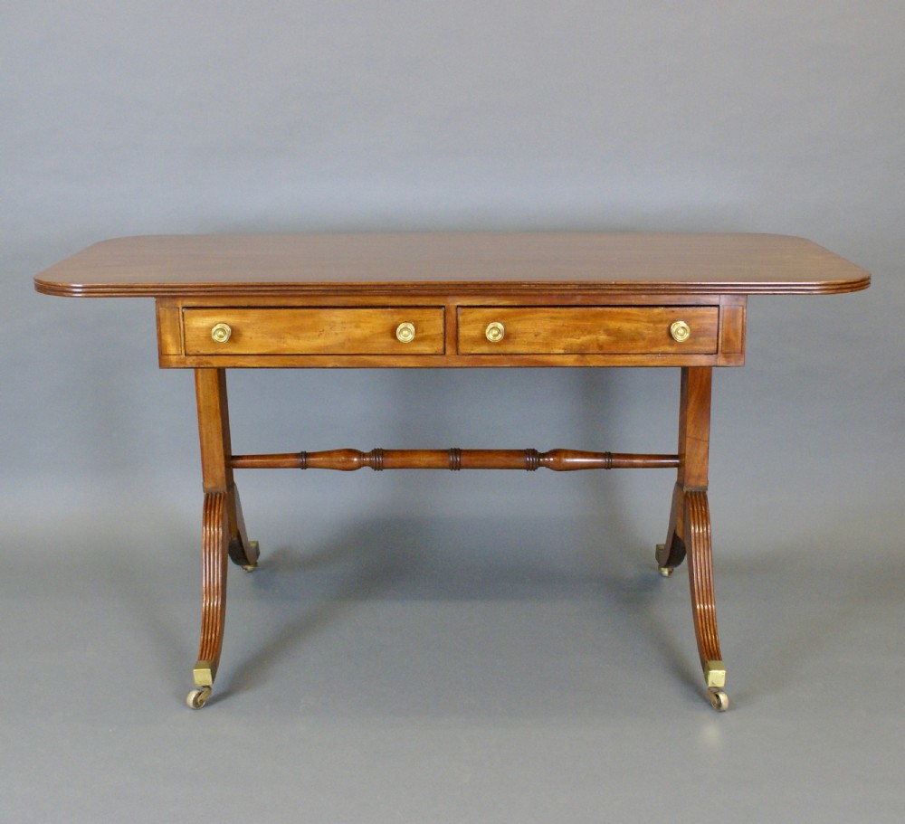 A Regency mahogany sofa table featuring two frieze drawers with brass knobs, reeded sabre legs on brass castors, and a turned stretcher. View VI