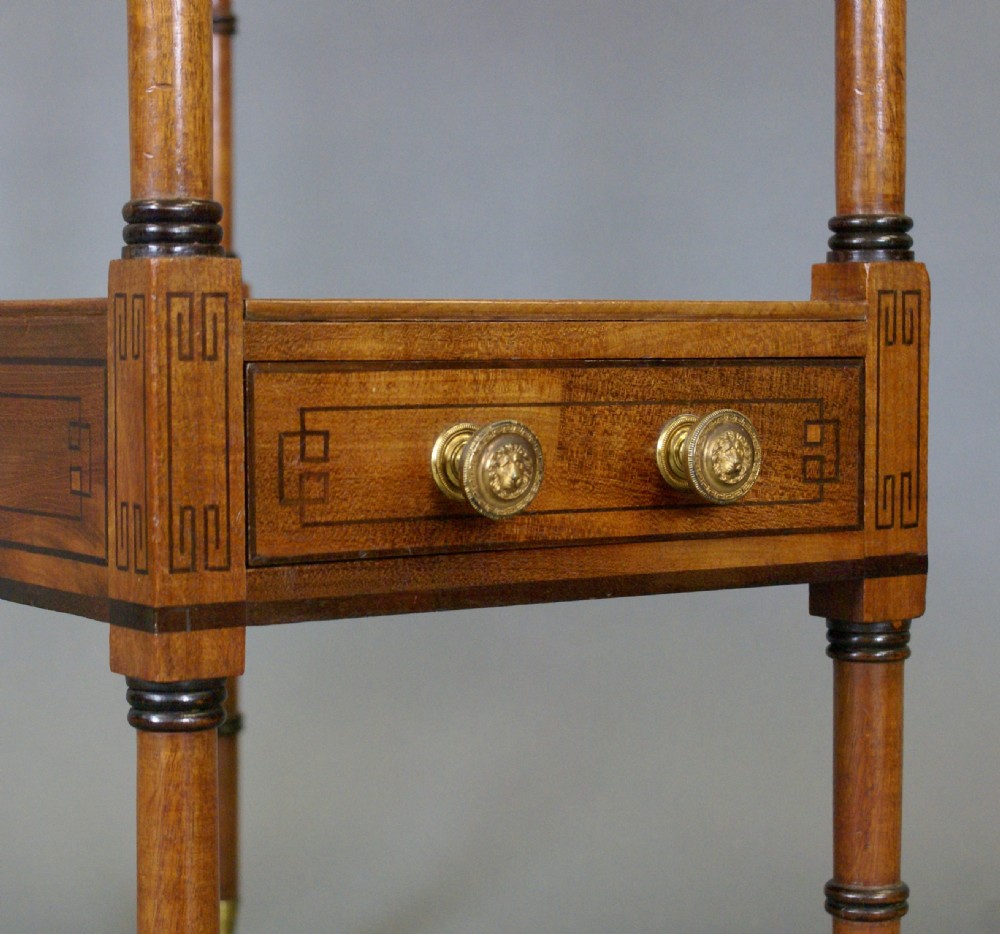 A Regency mahogany music Canterbury featuring a upper slatted compartment, a lower shelf above a single drawer with brass knobs, resting on turned legs with brass castors. View II