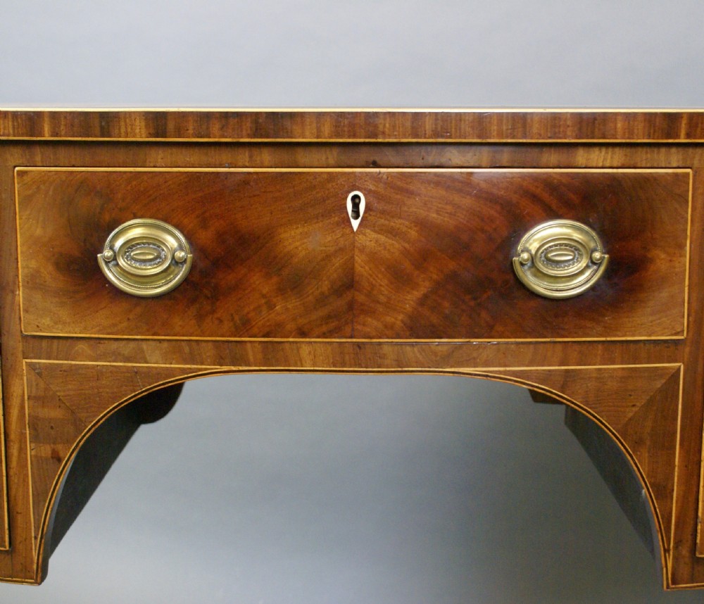 A George III mahogany sideboard featuring boxwood stringing, brass oval drop handles, a central arched apron, and tapered legs ending in spade feet. View V