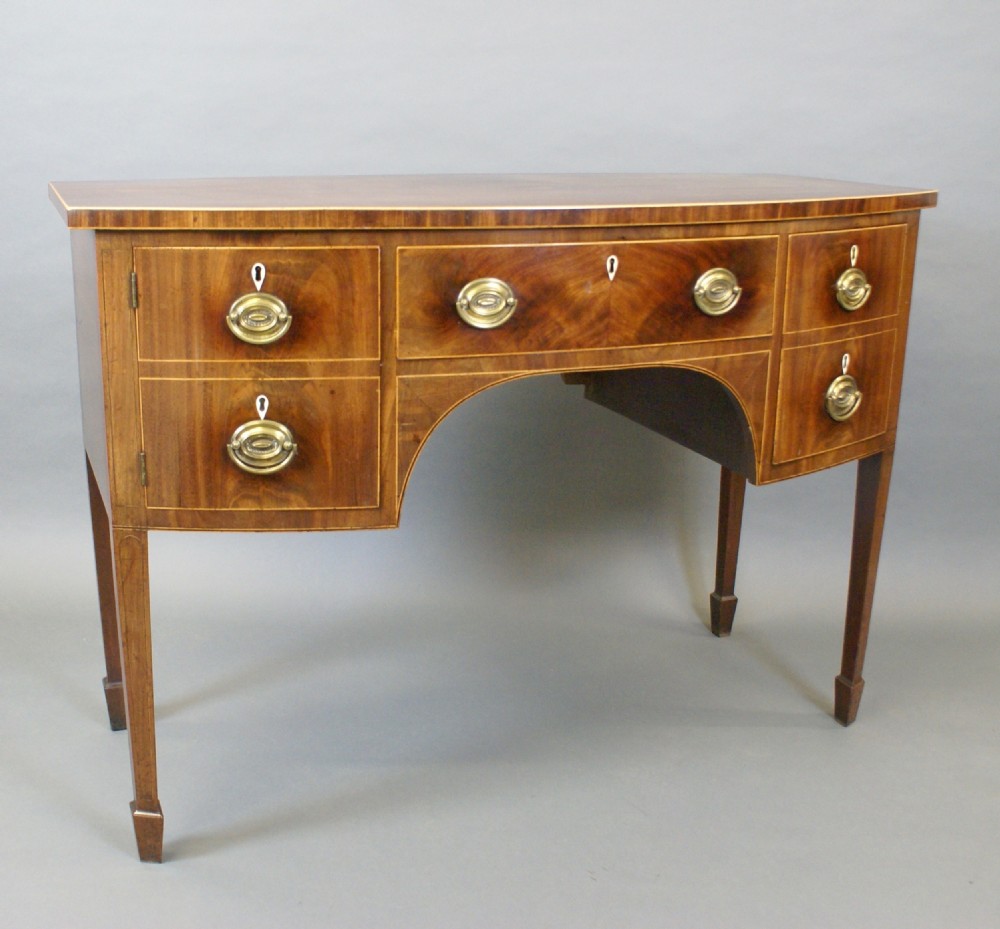 A George III mahogany sideboard featuring boxwood stringing, brass oval drop handles, a central arched apron, and tapered legs ending in spade feet. View VI