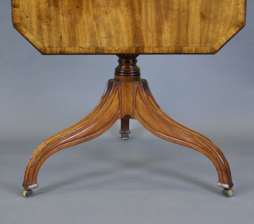 A Regency mahogany tilt-top table positioned upright on a turned tripod pedestal base with brass castors. View V