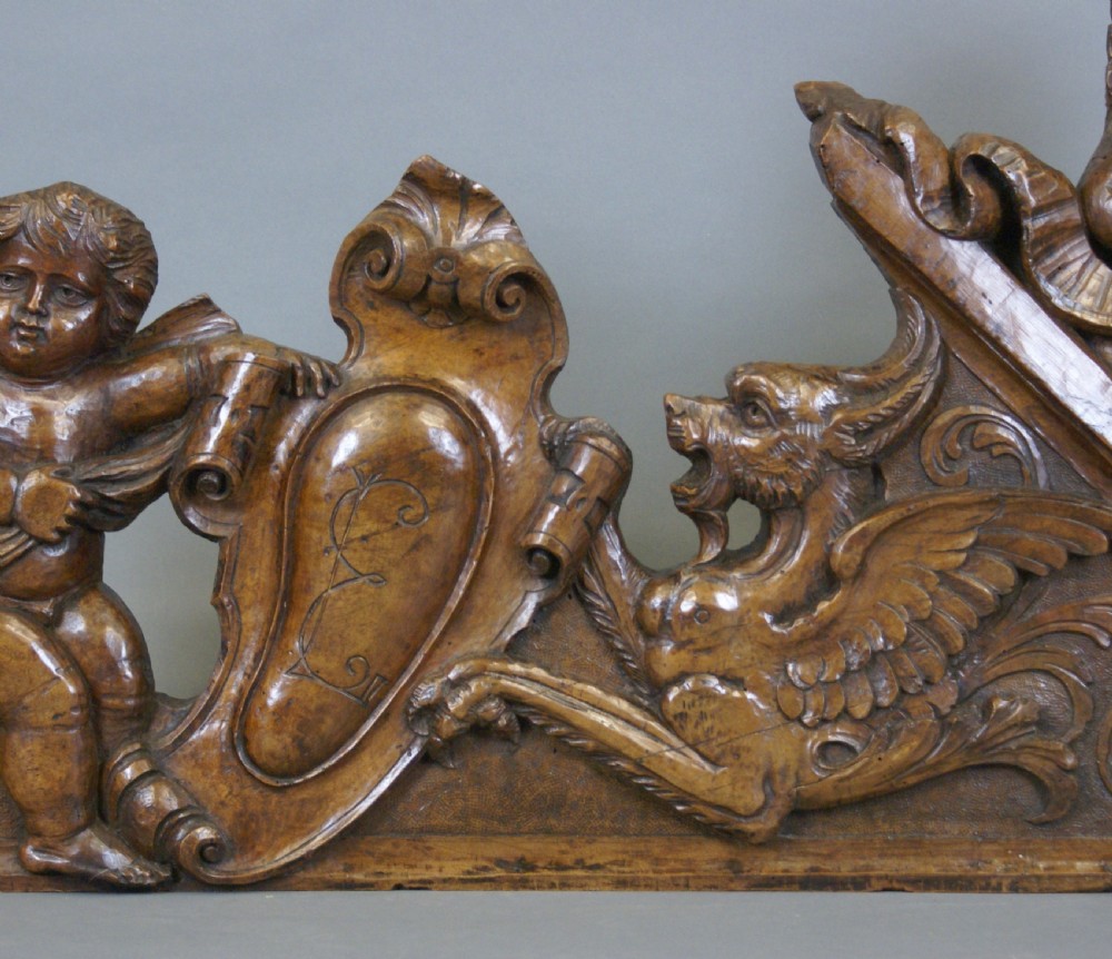A 17th-century carved walnut architectural relief featuring two sculpted putti figures, a central cartouche shield, and a winged mythical beast. View II