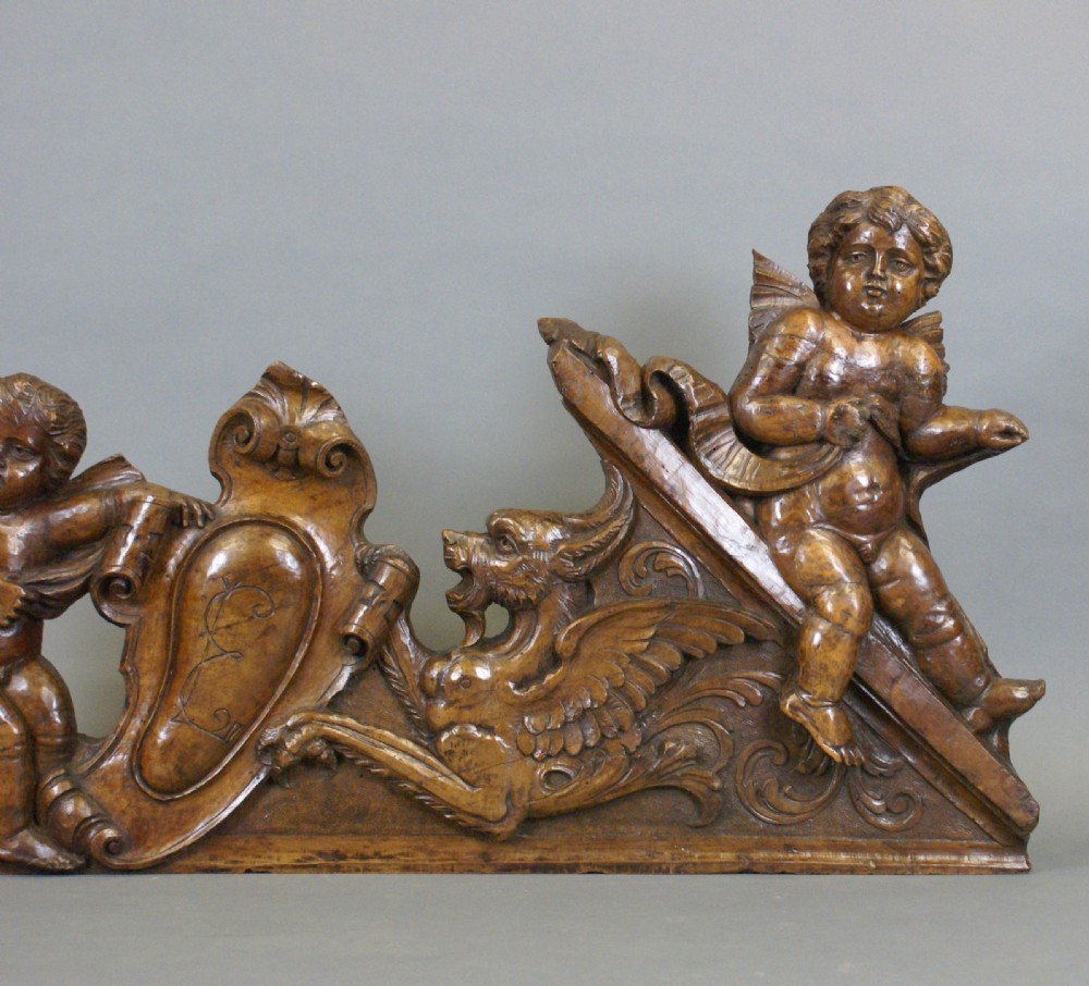 A 17th-century carved walnut architectural relief featuring two sculpted putti figures, a central cartouche shield, and a winged mythical beast. View III