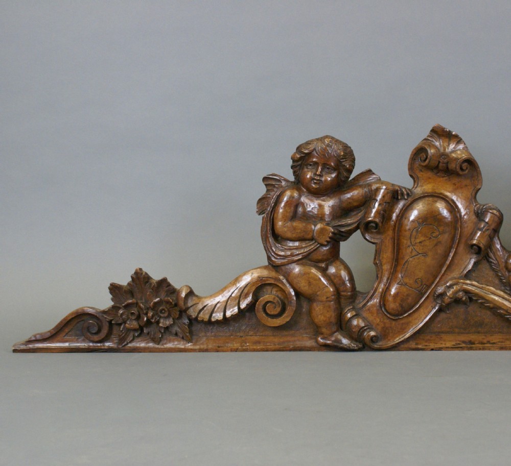 A 17th-century carved walnut architectural relief featuring two sculpted putti figures, a central cartouche shield, and a winged mythical beast. View V