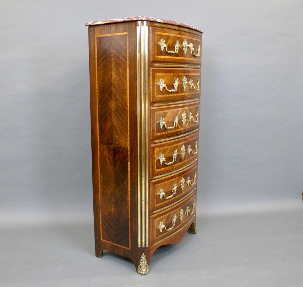 A tall French rosewood chest featuring geometric parquetry inlay, six drawers with gilt brass handles, fluted corner columns, and a shaped pink marble top. View VI