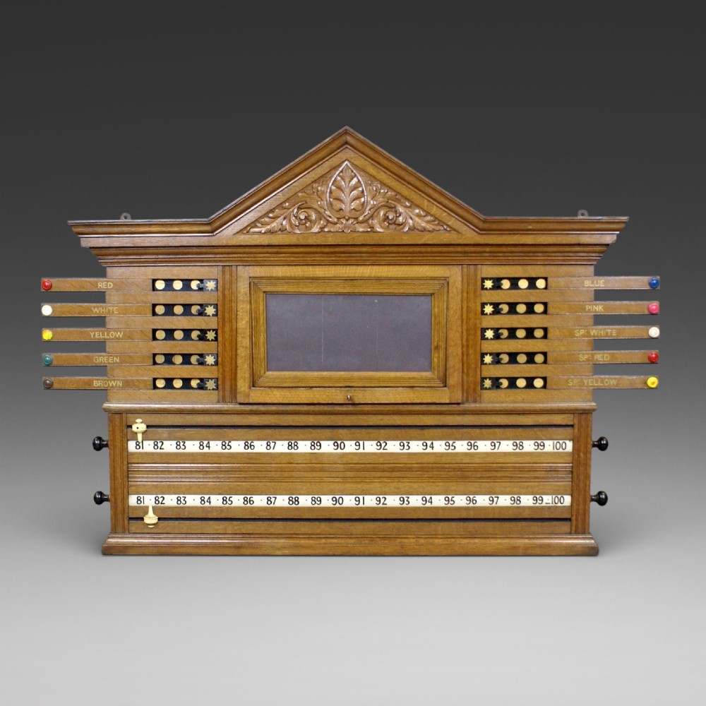 An antique pale oak wall-mounted snooker scoreboard featuring a carved pediment, sliding colour markers, central slate panel, and numbered rolling dials.