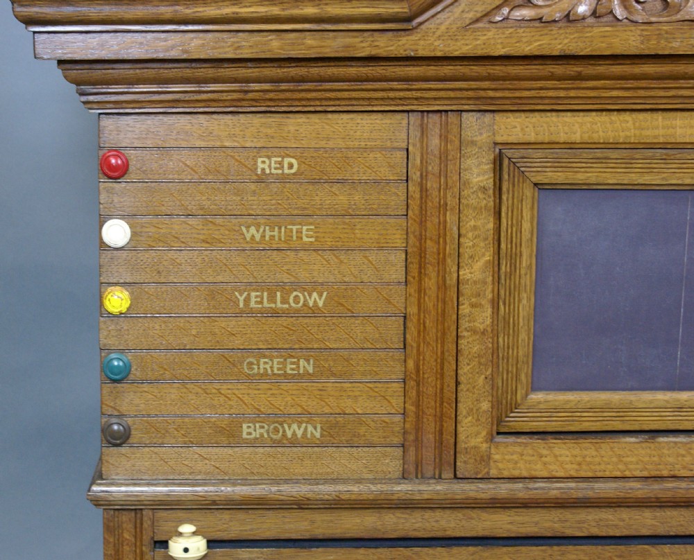 An antique pale oak wall-mounted snooker scoreboard featuring a carved pediment, sliding colour markers, central slate panel, and numbered rolling dials. View V