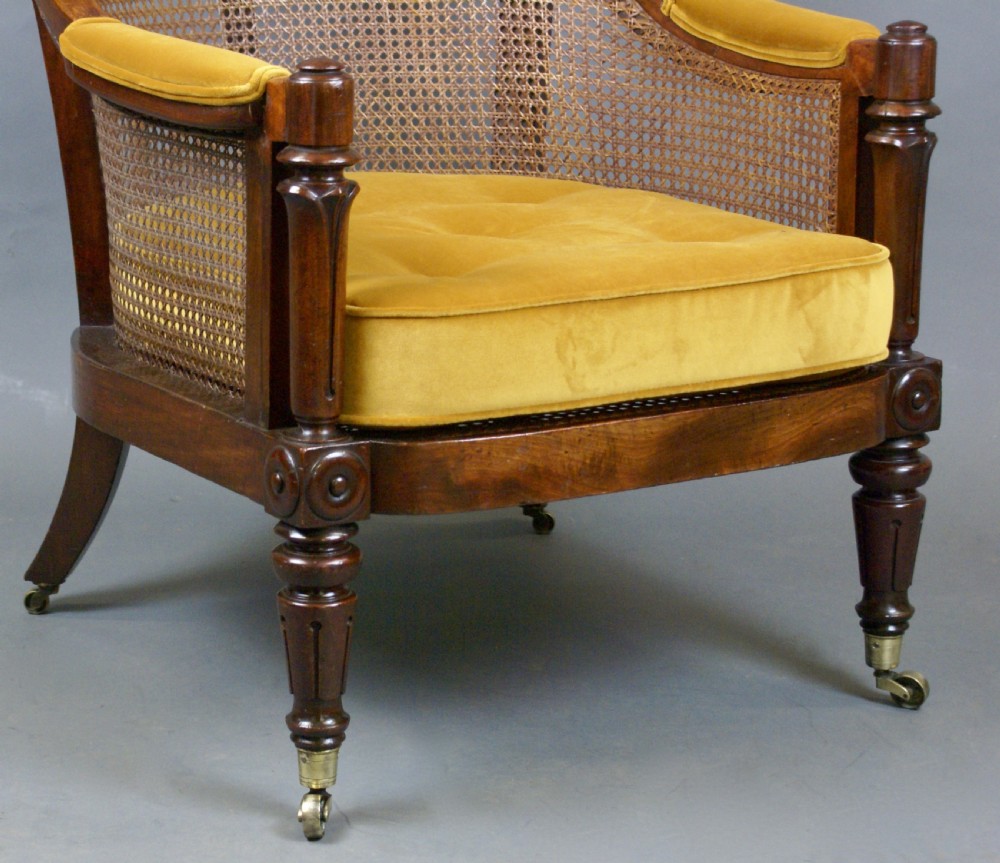A Regency mahogany bergere chair featuring a woven cane back and sides, turned front legs with brass castors, and a gold velvet seat cushion. View VI