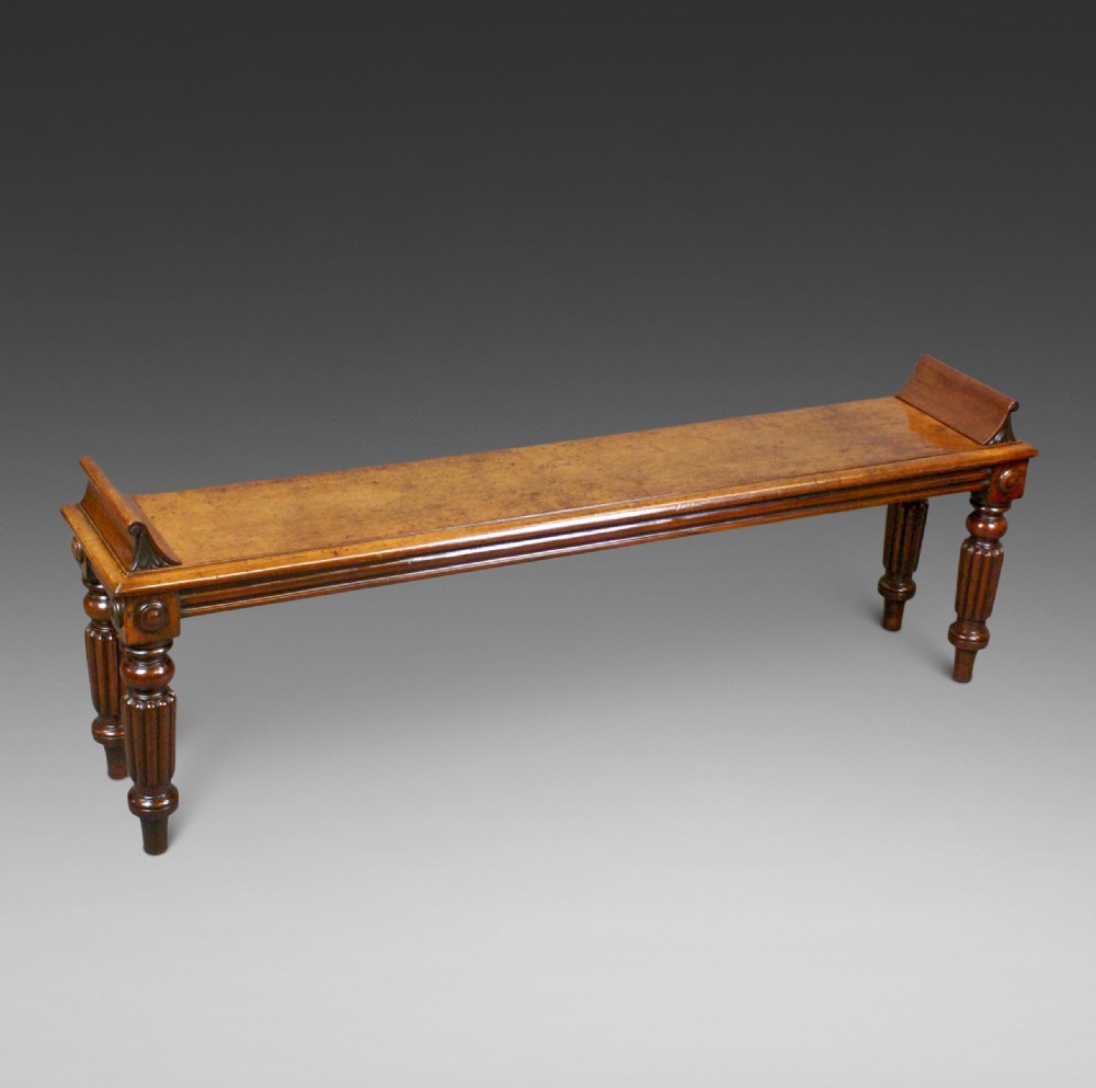 An antique wooden window seat with fluted turned legs and scroll ends on a neutral background.