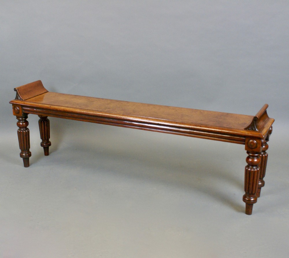 An antique wooden window seat with fluted turned legs and scroll ends on a neutral background. View II