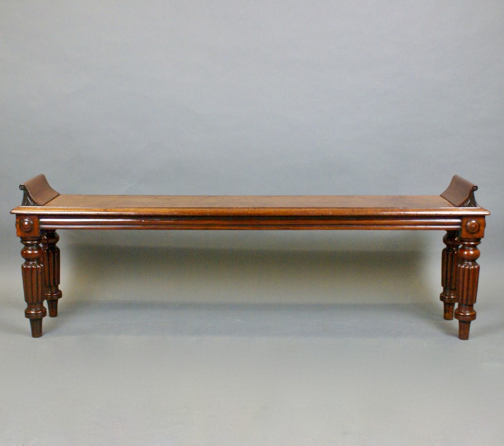 An antique wooden window seat with fluted turned legs and scroll ends on a neutral background. View VIII