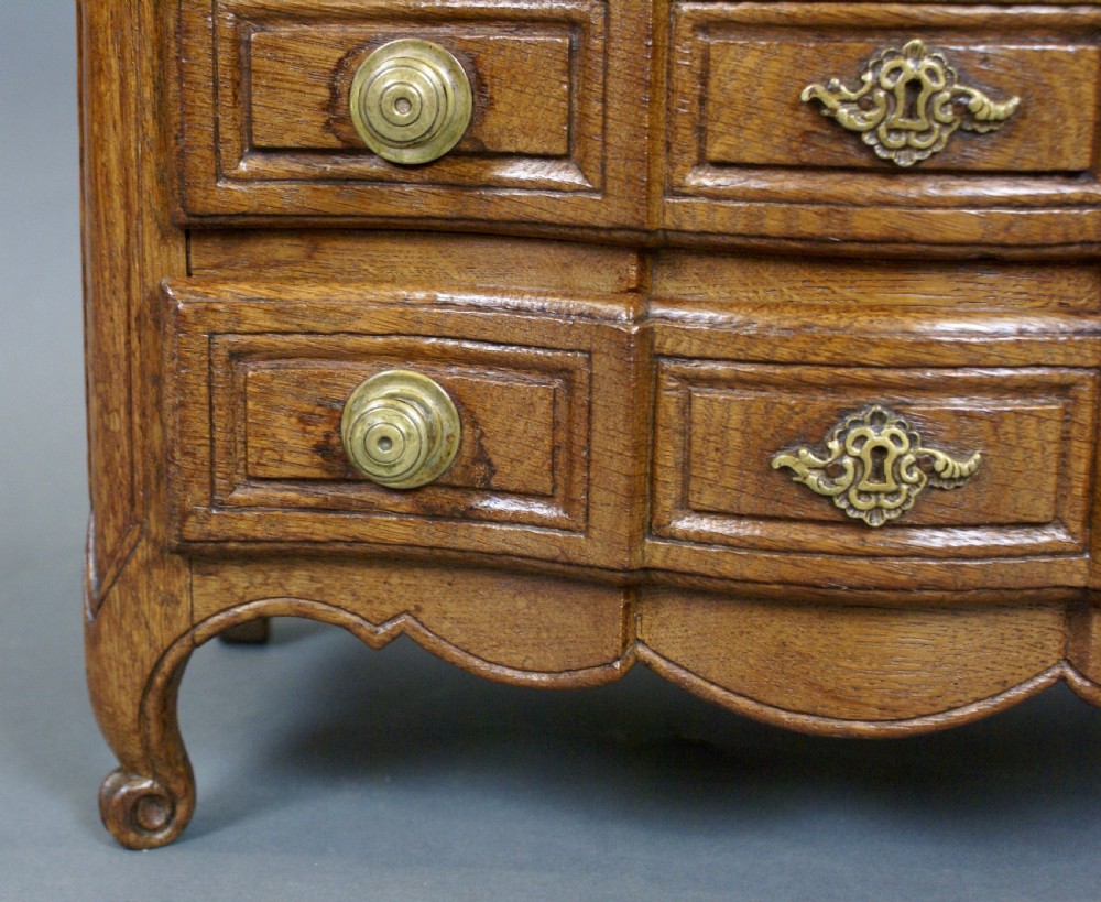 A 19th-century French miniature oak commode featuring a serpentine front, three moulded drawers with brass hardware, and short cabriole legs. View IV