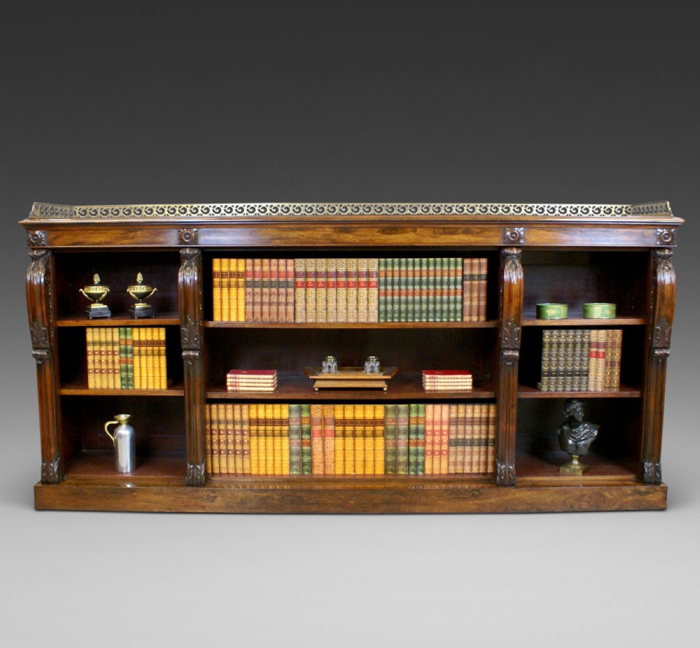 A low Regency rosewood open bookcase featuring three bay shelf sections, carved corbels, and a pierced brass top gallery.