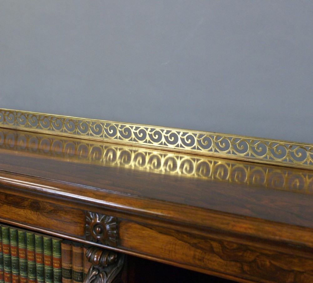 A low Regency rosewood open bookcase featuring three bay shelf sections, carved corbels, and a pierced brass top gallery. View V