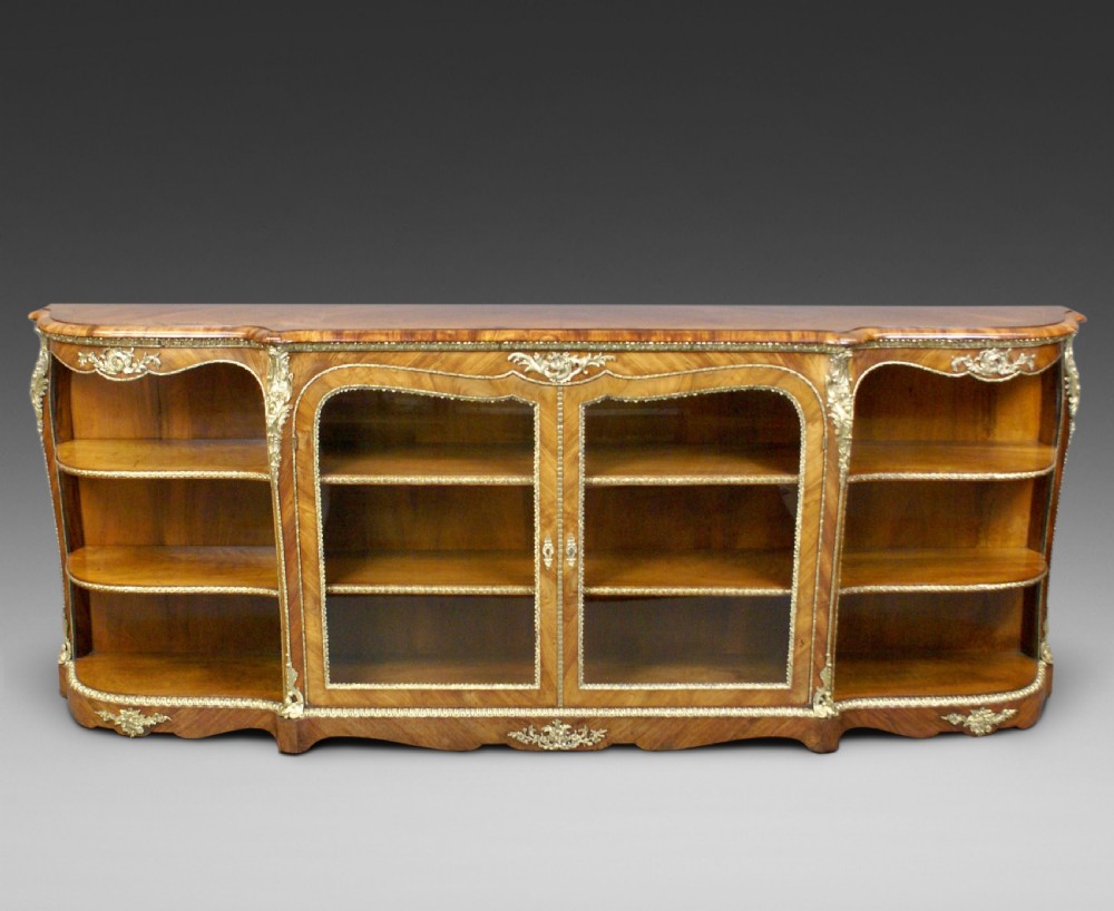 An antique walnut side cabinet featuring central glazed double doors flanked by open curved side shelves and gilt-bronze mounts.