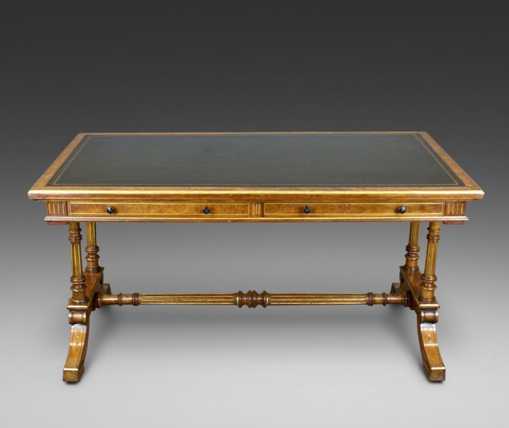 A Victorian burr walnut library writing table featuring a dark green leather inset surface, frieze drawers, turned support legs, and a central stretcher.