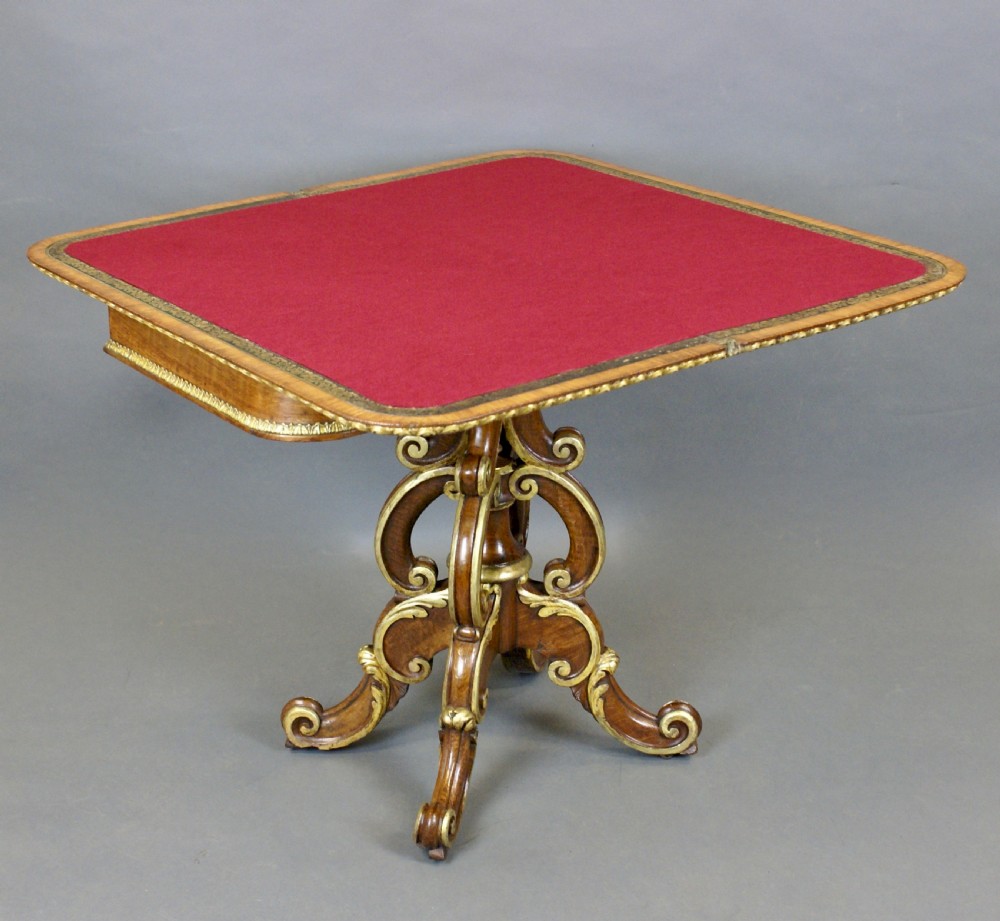 A Victorian walnut card table featuring gilt leaf moulding, a fold-over top, and a carved scrollwork pedestal base. View VI