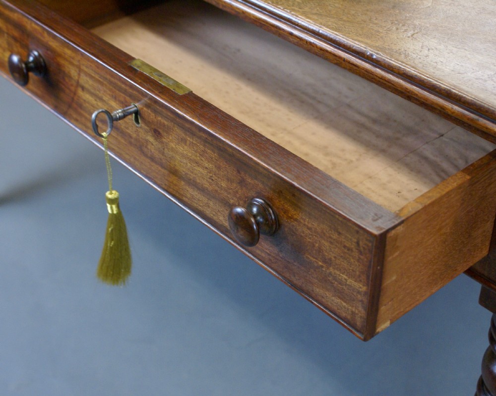 A rectangular late George III mahogany partners writing table featuring frieze drawers with wooden knob handles and turned legs ending in brass castors. View V