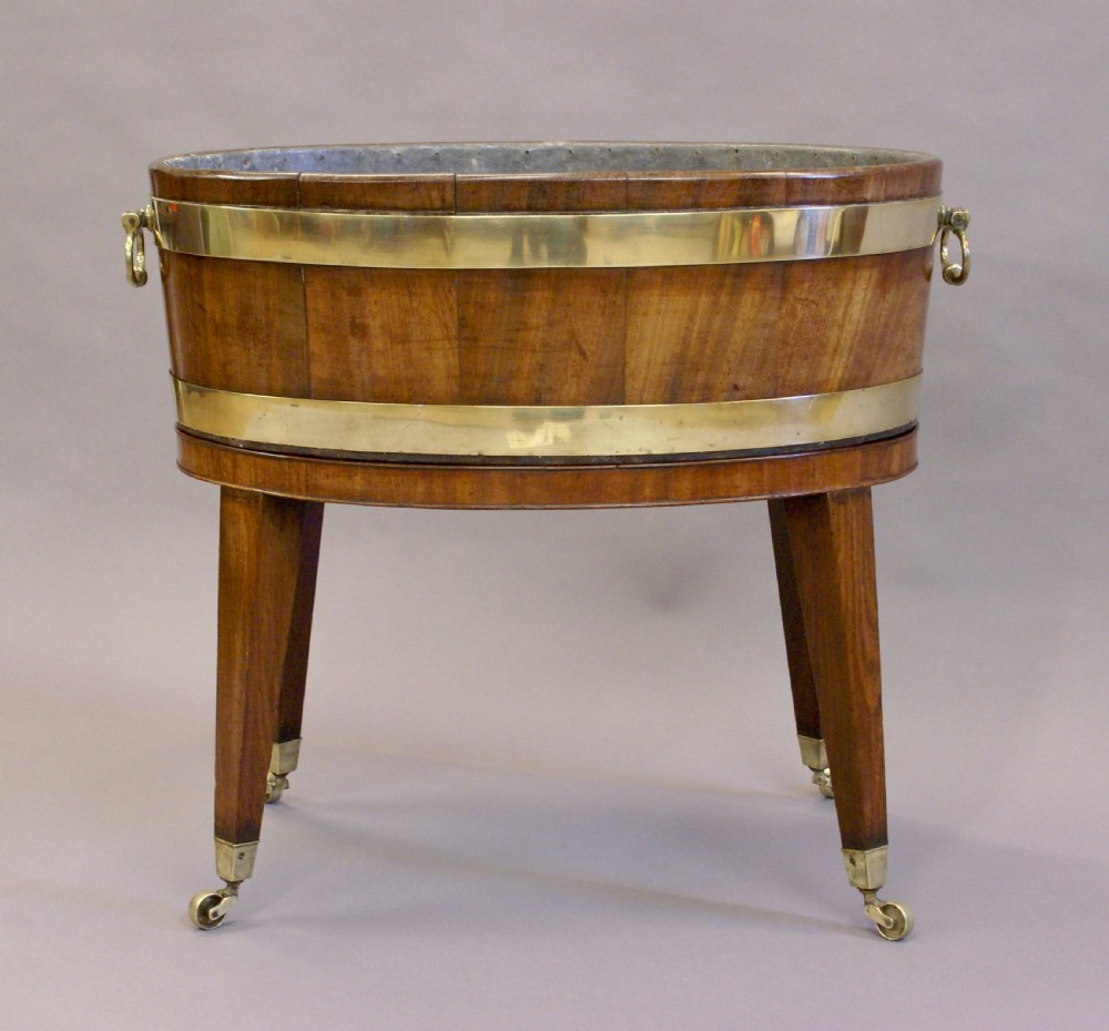 A George III oval mahogany wine cooler featuring brass binding hoops, twin handles, and tapered square legs on brass castors. View II