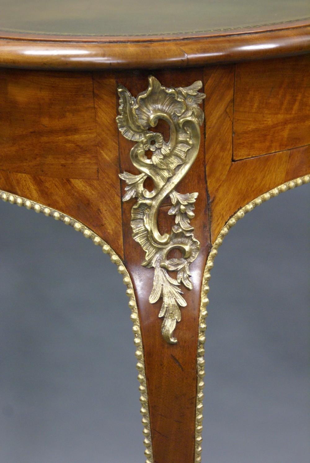 A George IV satinwood writing table featuring a green leather inset top, gilt-bronze ormolu mounts, and slender cabriole legs. View III