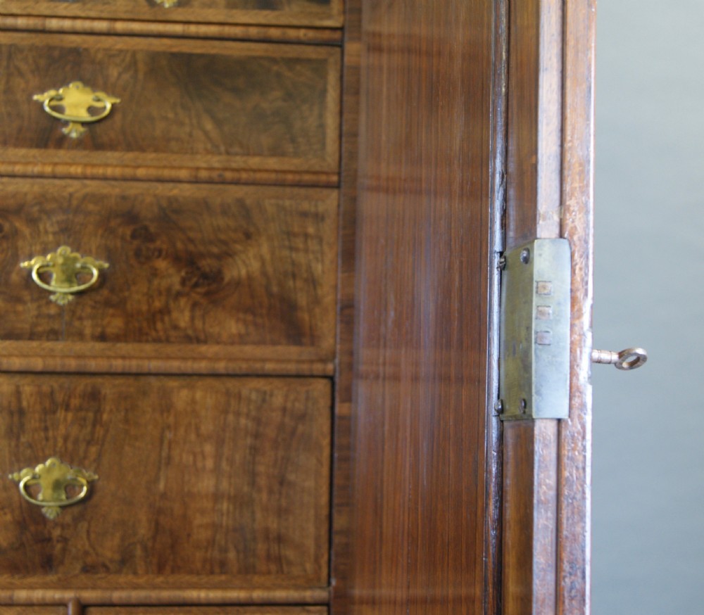 A George I figured walnut secretaire cabinet featuring a moulded upper section with two mirrored doors above a chest of drawers with brass drop handles. View V
