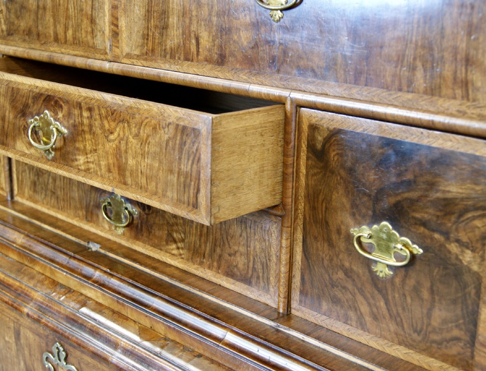 A George I figured walnut secretaire cabinet featuring a moulded upper section with two mirrored doors above a chest of drawers with brass drop handles. View VI