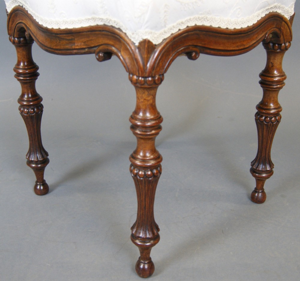 A 19th-century rosewood stool featuring four intricately turned fluted legs, a carved shaped apron, and a light cream patterned upholstered seat with braided edge trim. View III