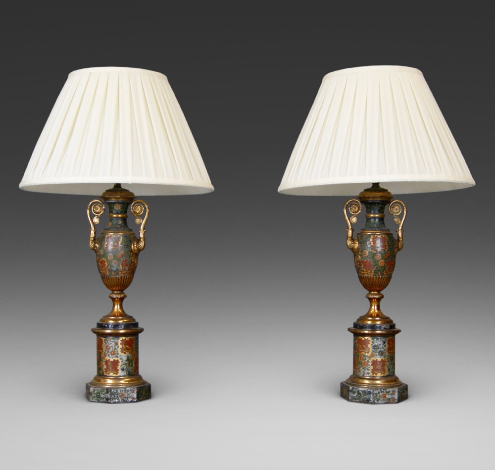 A pair of French classical urn-shaped toleware table lamps featuring hand-painted floral decoration, gilded scroll handles, octagonal pedestals, and pleated cream shades.