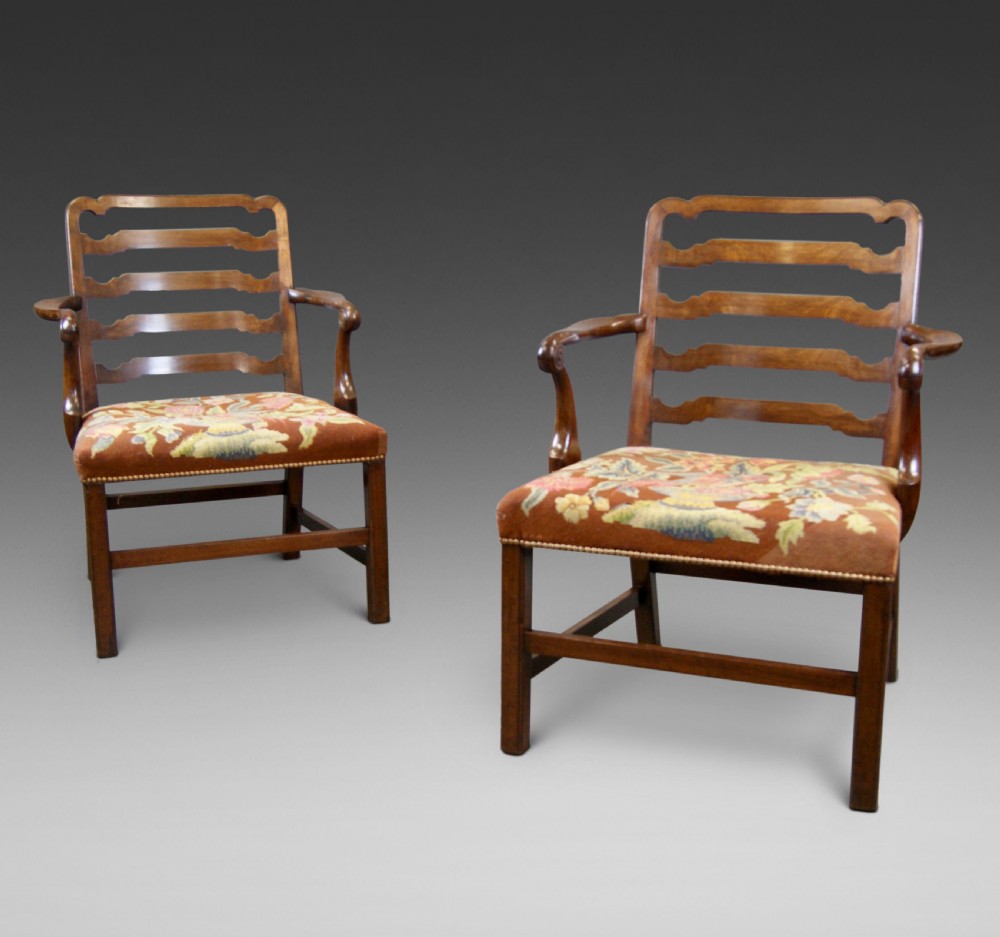A pair of mahogany Chippendale ladderback armchairs with curved open arms and floral needlepoint seats.