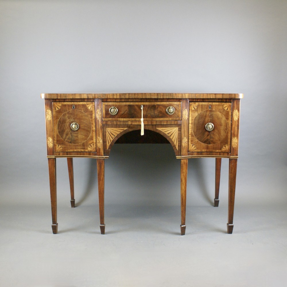 A late 18th-century mahogany serpentine sideboard featuring inlaid fan motifs, three drawers, an arched central apron, and four tapered square legs with spade feet. View VII