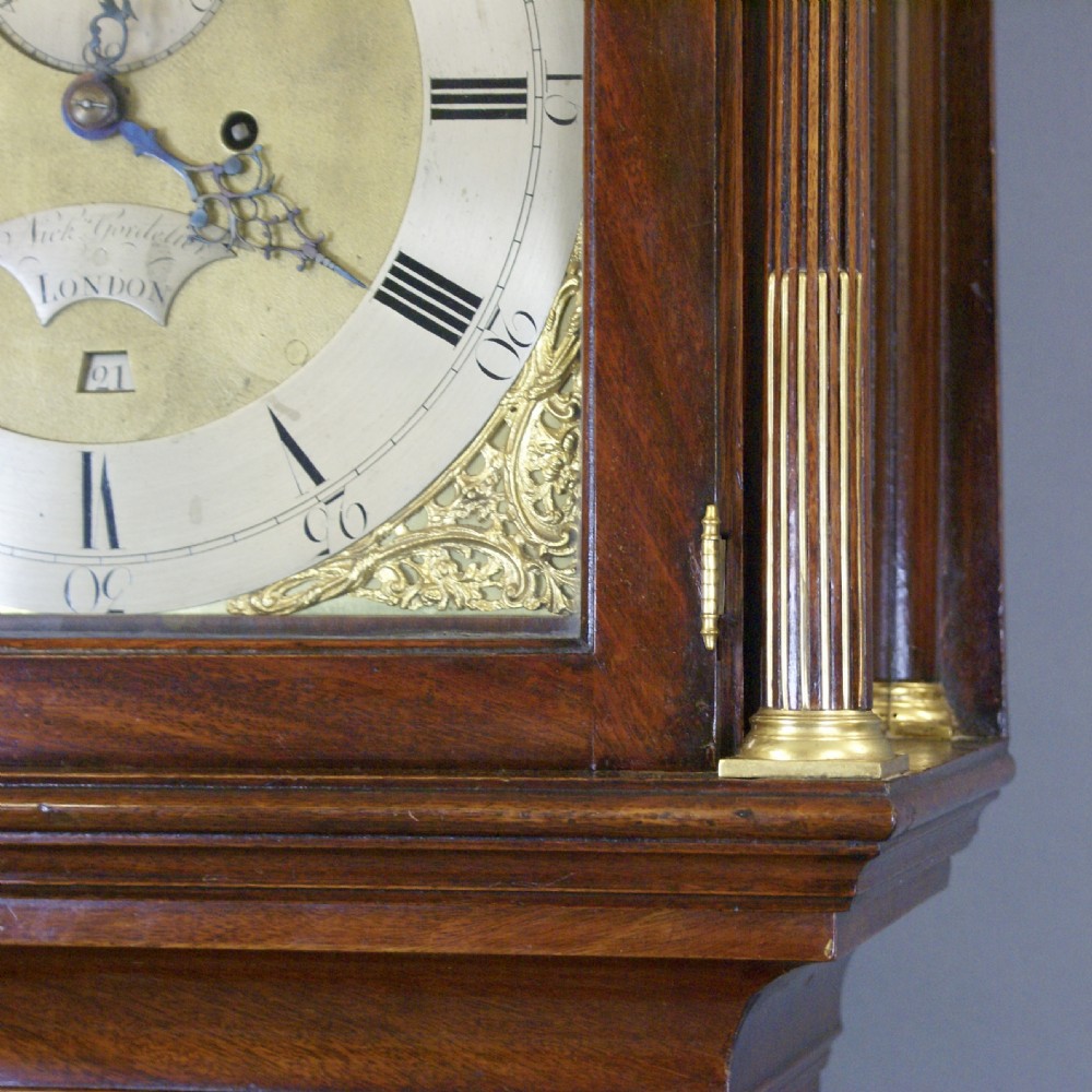 An antique Georgian mahogany longcase clock featuring an arched brass dial, fluted columns, eagle finials, and a flame mahogany trunk door. View VIII