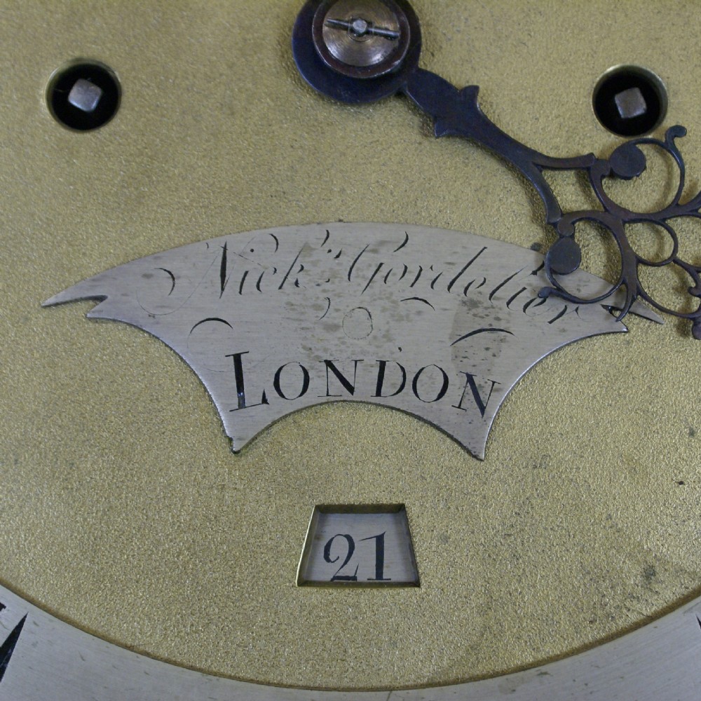An antique Georgian mahogany longcase clock featuring an arched brass dial, fluted columns, eagle finials, and a flame mahogany trunk door. View IX