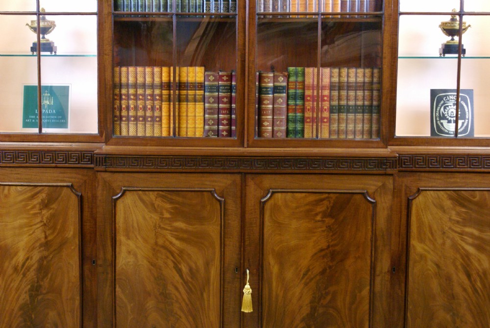 A George III mahogany breakfront bookcase featuring astragal glazed upper doors, a swan-neck pediment, and flame mahogany panelled lower cupboard doors. View III
